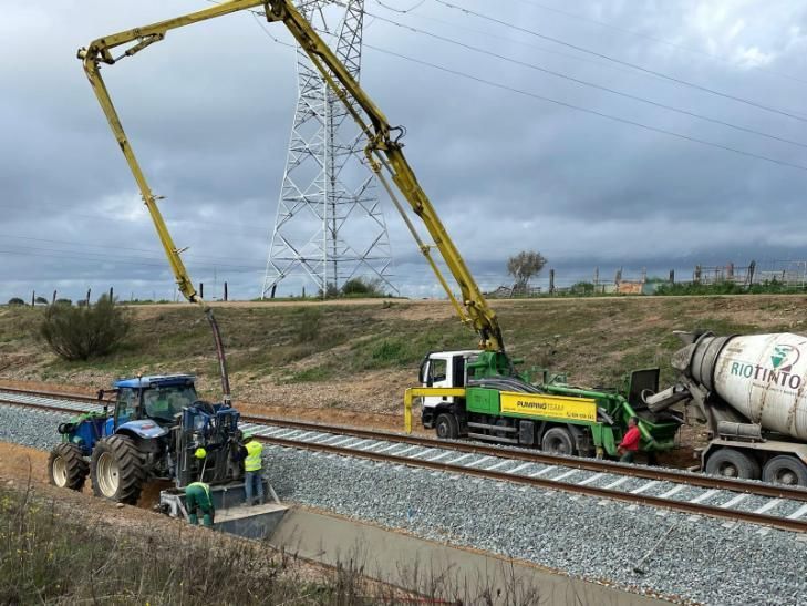 Se vierte hormigón para construir el ferrocarril con un camión bomba y un tractor en un día nublado.