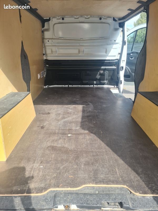 Une Peugeot 206+ blanche garée sur un parking gravillonné à côté d'un drapeau publicitaire jaune