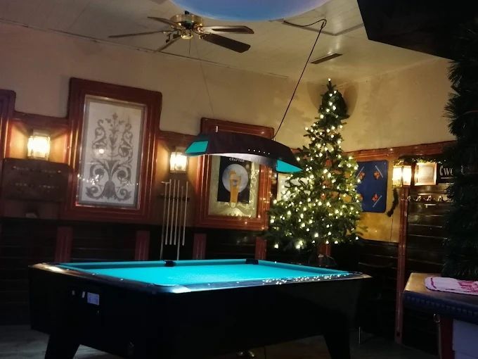 Dunkles Billardzimmer mit Billardtisch, Weihnachtsbaum und Wandleuchten