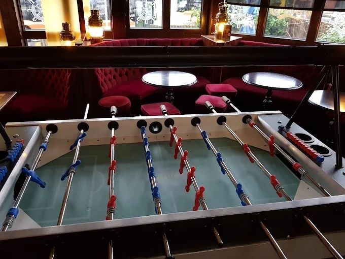 Tischfussballtisch in einer schwach beleuchteten Lounge mit roten Sitzen und weissen Tischen im Hintergrund