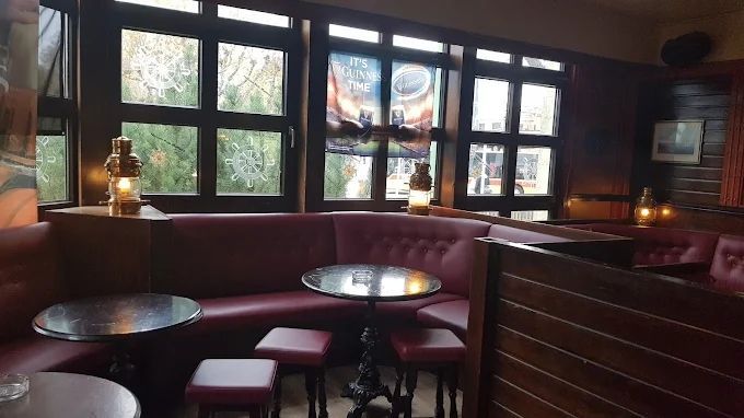 Gemütlich beleuchtete Bar-Lounge mit burgunderroten Sitznischen, runden Tischen, Hockern und Fenstern mit Blick auf eine Strasse.
