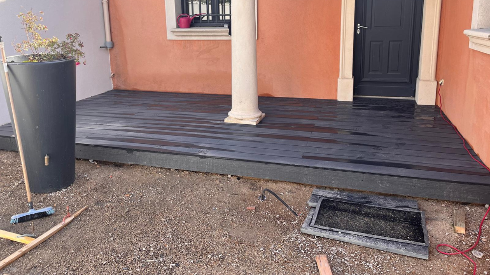 Terrasse noire avec une colonne, une porte, une jardinière et du gravier.