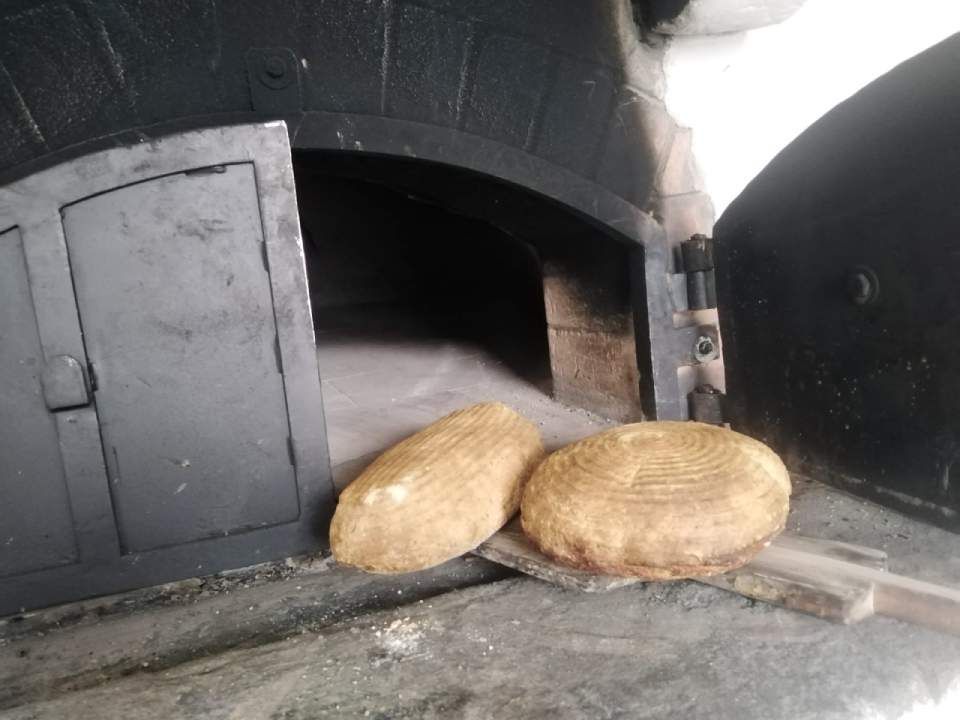Zwei Brote auf einem Holzschieber vor einem dunklen, offenen Ofen.
