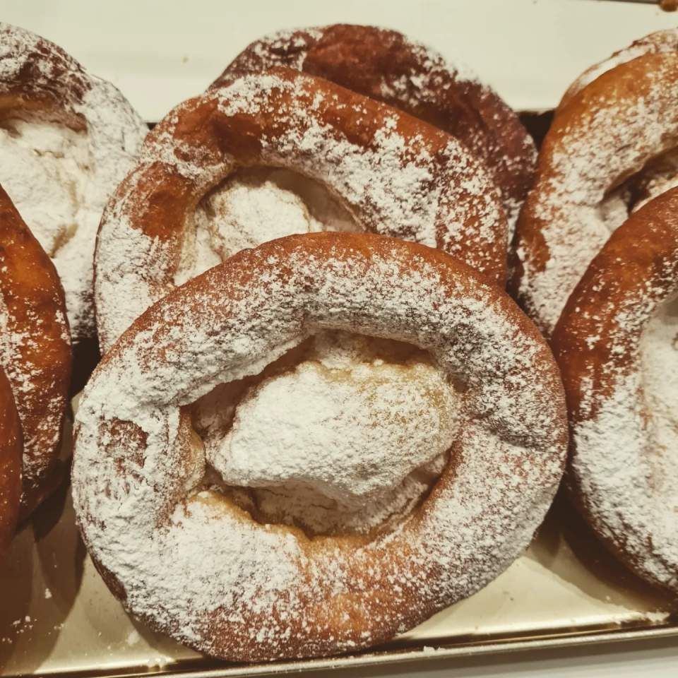 Auf einem Tablett angerichtete, mit Puderzucker bestäubte, frittierte Teigwaren.