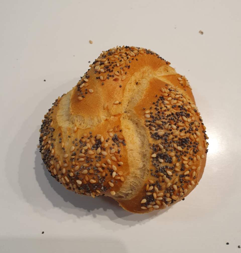 Nahaufnahme eines mit Sesam und Mohn bestreuten Kaiserbrötchens auf weißem Untergrund.