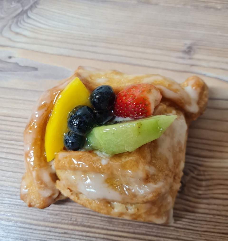 Glasiertes Gebäck mit frischen Früchten (Mango, Blaubeeren, Erdbeeren, Kiwi) auf einer Holzoberfläche.
