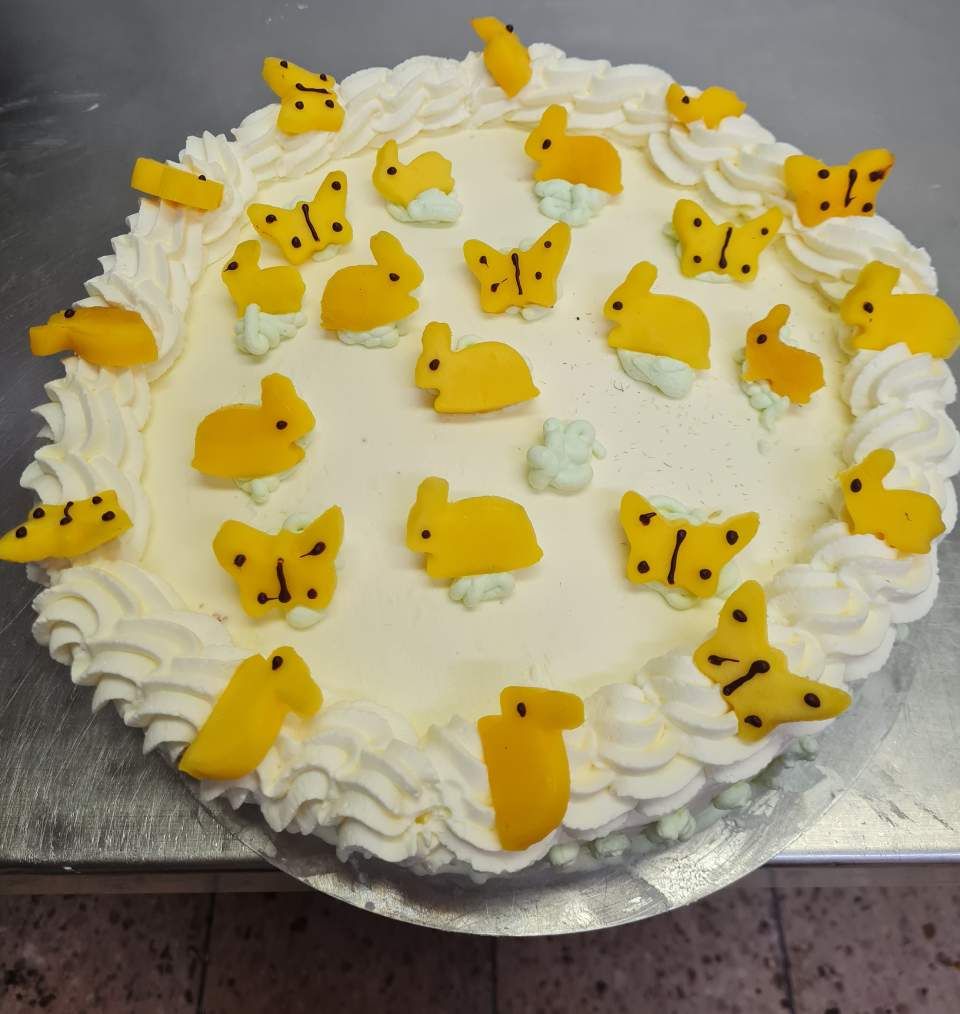 Eine Torte, verziert mit gelben Hasen und Schmetterlingen auf weißem Zuckerguss, umgeben von Schlagsahne.