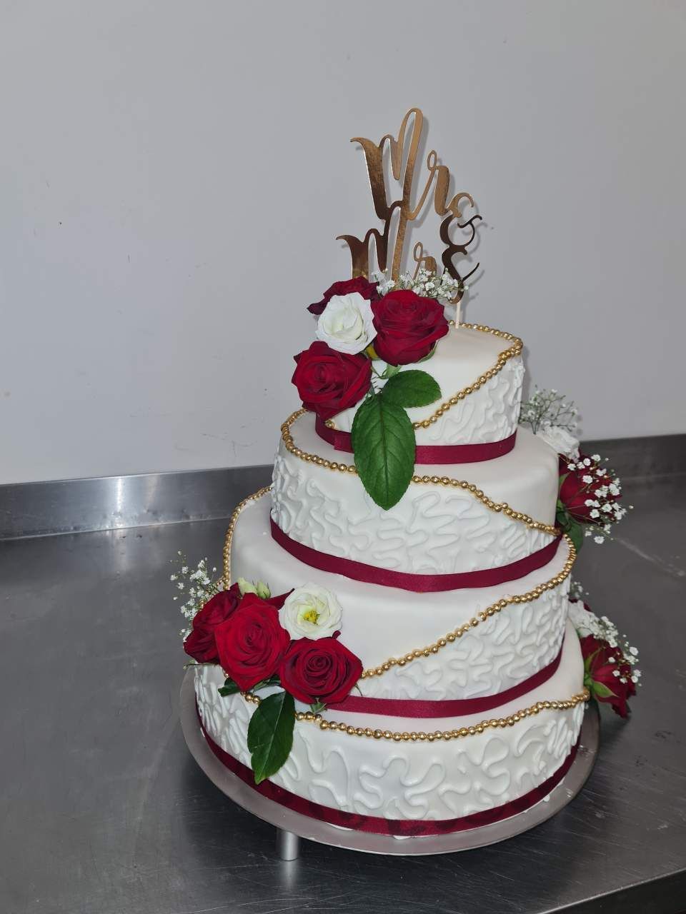 Dreistöckige Hochzeitstorte mit roten Rosen, goldenen Kettenverzierungen und der Aufschrift „Mr & Mrs“.