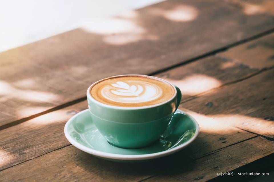 Latte in einer türkisfarbenen Tasse mit Latte Art auf einem Holztisch, gefiltertes Sonnenlicht.