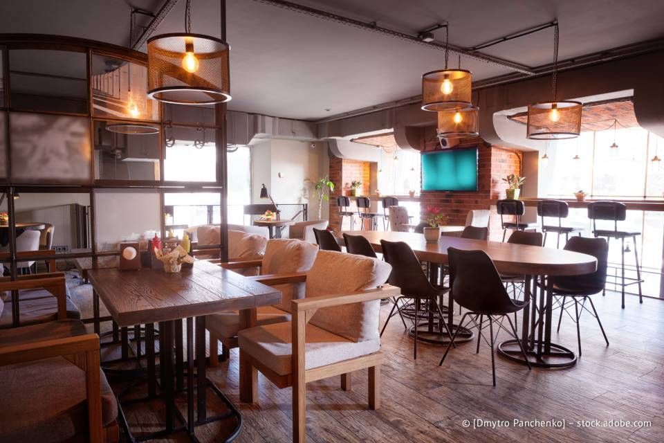 Restaurantinterieur mit Tischen, Stühlen und Hängelampen; im Hintergrund eine freigelegte Backsteinwand.