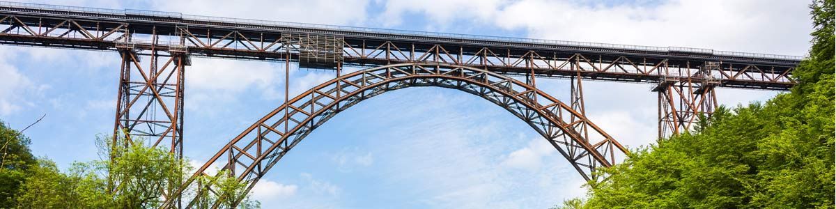 Eine Brücke über einen Fluss mit Bäumen im Vordergrund und einem blauen Himmel im Hintergrund.