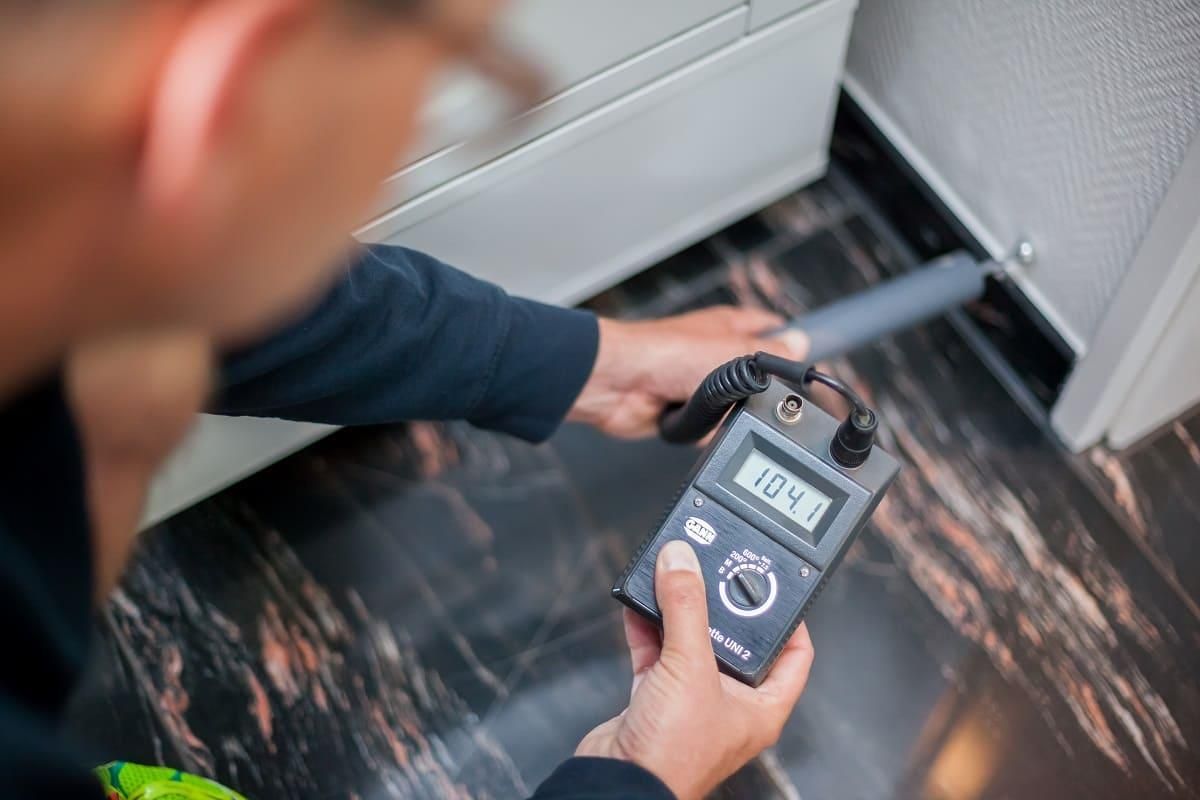 Ein Mann misst mit einem digitalen Thermometer die Temperatur eines Raumes.