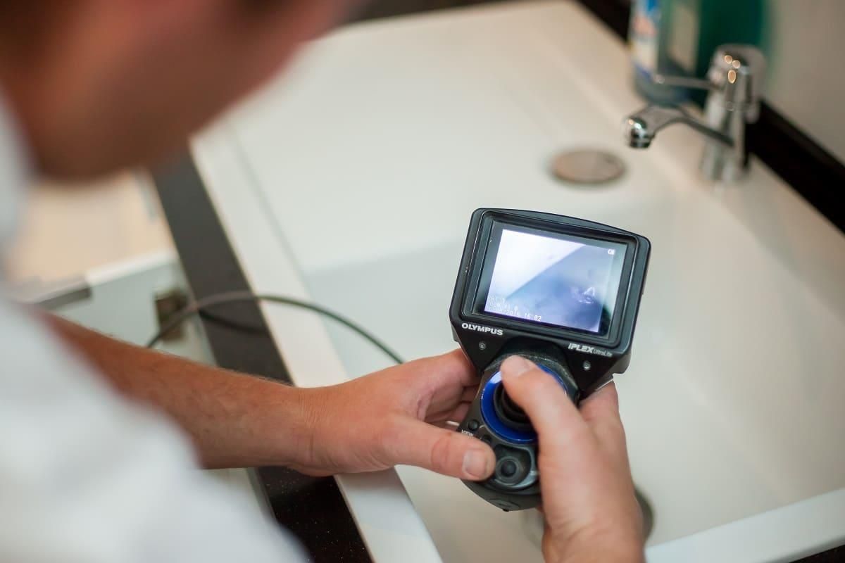 Ein Mann hält eine Kamera vor einem Waschbecken.