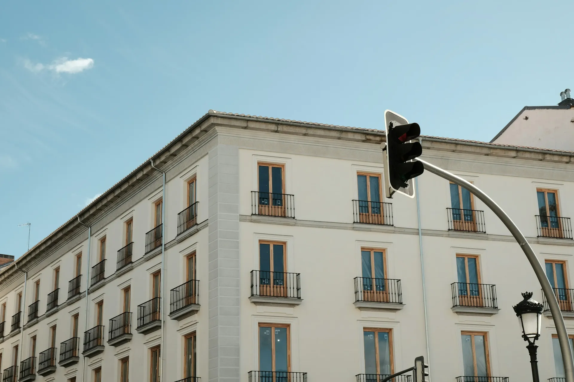 Edificio blanco con múltiples ventanas y balcones bajo un cielo azul claro; semáforo en primer plano.