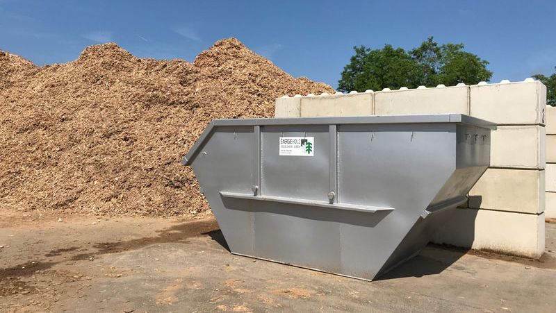 Metallmüllcontainer neben einem Haufen Holzspäne und Betonblöcke, im Freien.