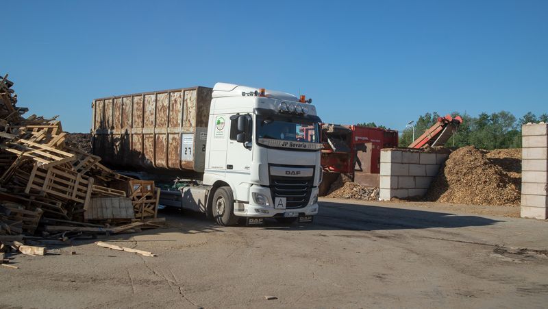 Weißer LKW mit einem mit Holzabfällen beladenen Container in einer Recyclinganlage im Freien.