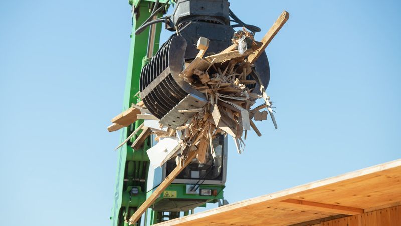 Grüne Kranichklaue hält Trümmer einer Dekonstruktion vor einem klaren blauen Himmel.