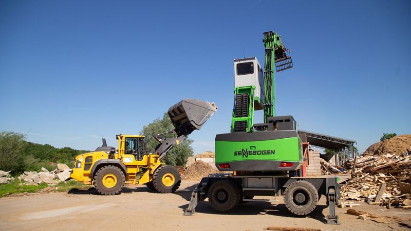 Gelber Lader und grüner Materialtransporter arbeiten an einem sonnigen Tag auf einer Baustelle zusammen.
