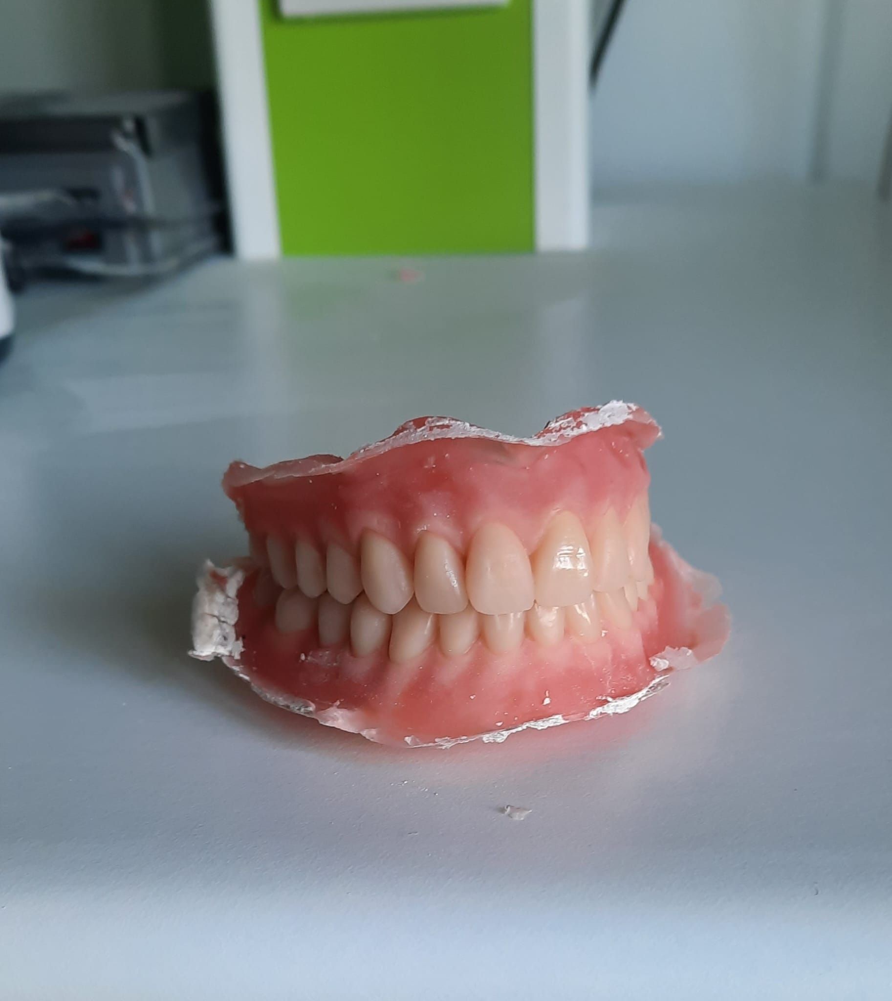 Un modelo dental rosa de dientes superiores e inferiores sobre una mesa blanca, con un fondo verde desenfocado.