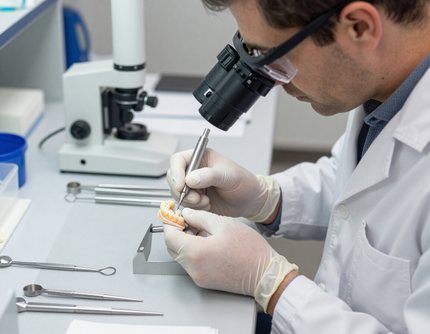Científico con bata de laboratorio que utiliza un microscopio y unas pinzas para examinar una muestra en una mesa de trabajo