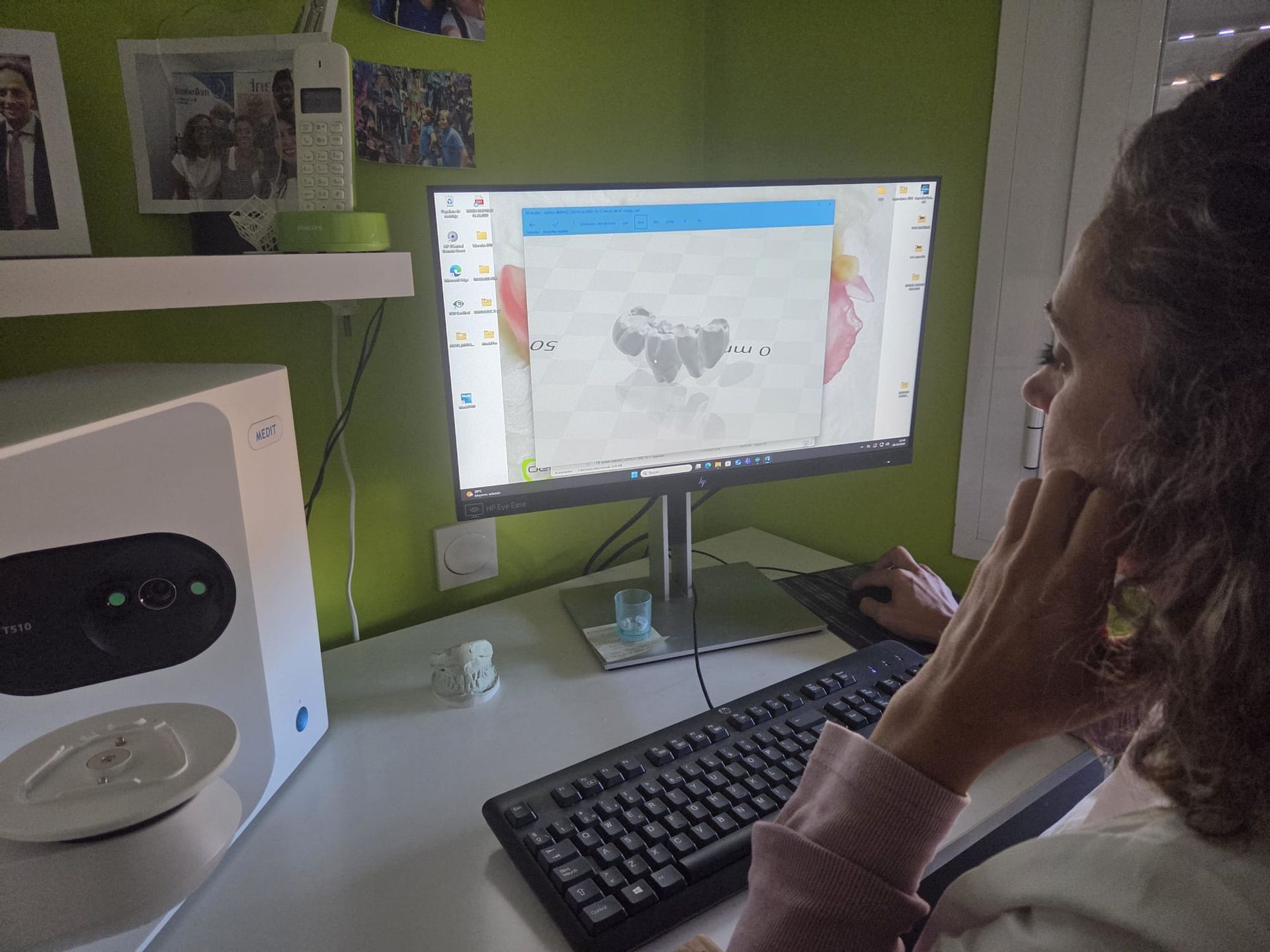 Una persona usando un ordenador de sobremesa en un escritorio, en una habitación verde, con un teclado, un monitor y un altavoz cerca.