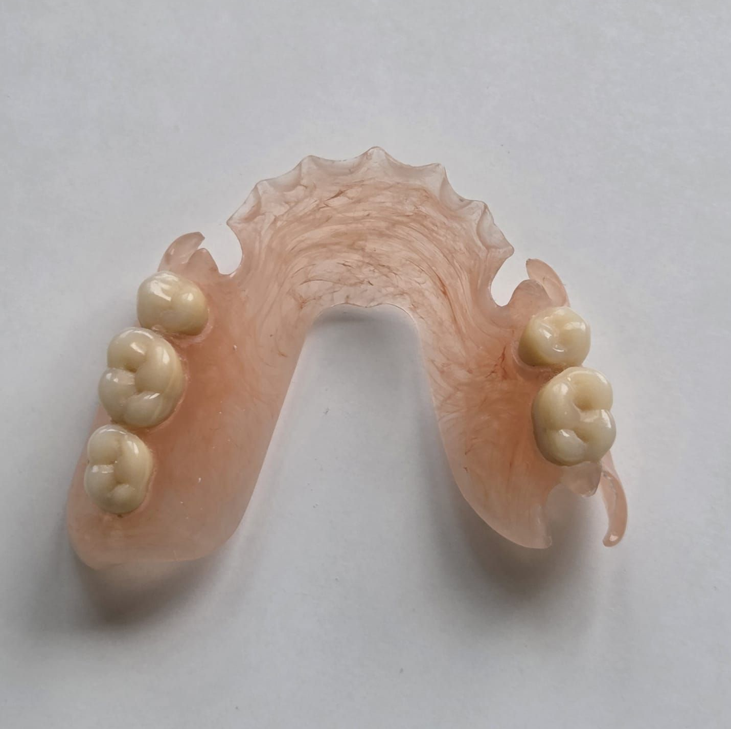 Prótesis dental parcial rosa con varios dientes postizos blancos sobre un fondo claro