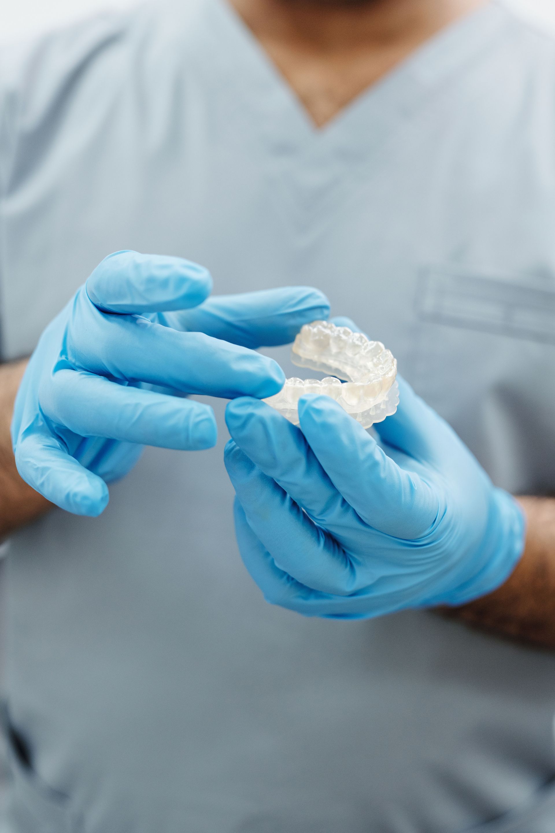 Manos enguantadas sosteniendo e inspeccionando un molde dental transparente