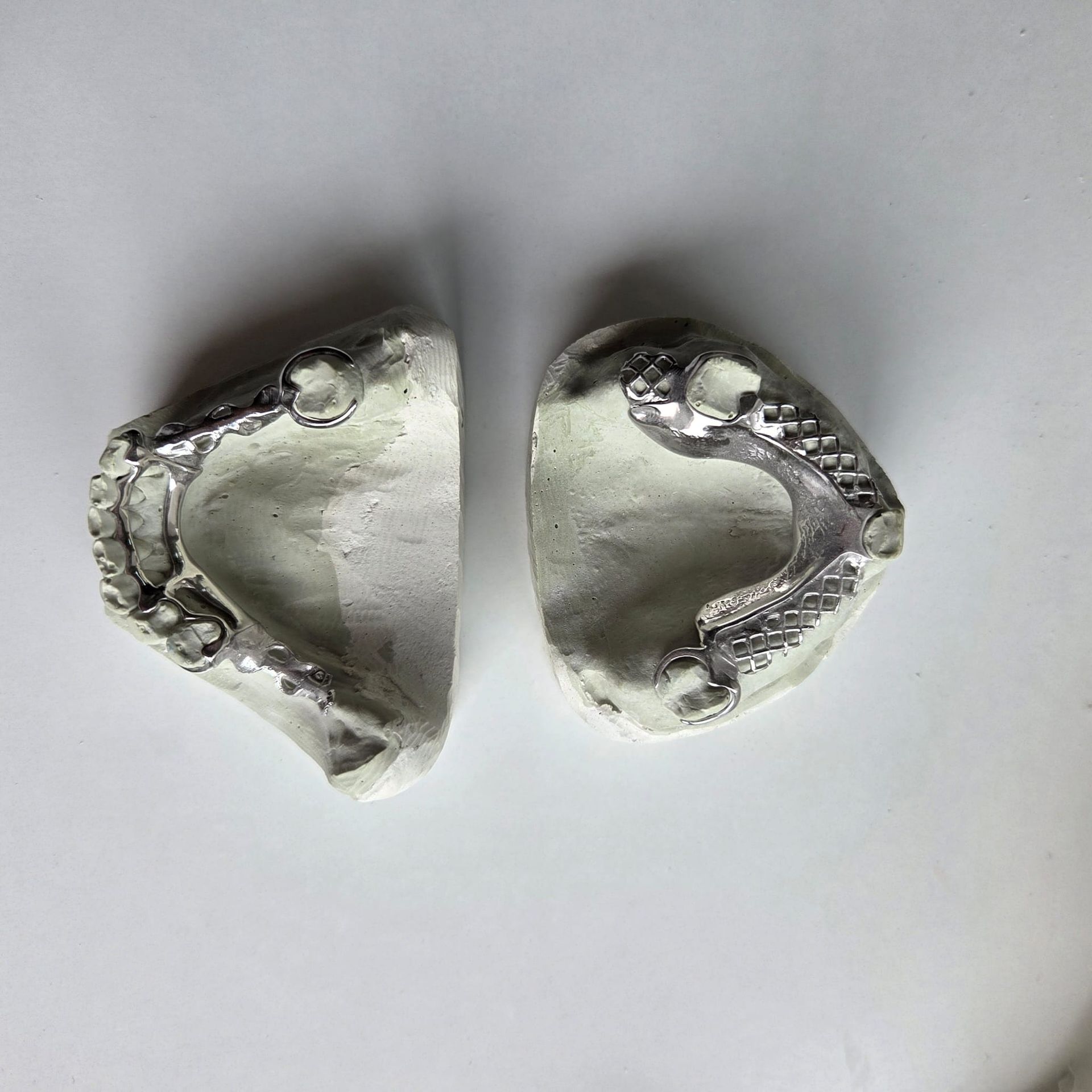 Un dentista da forma a un modelo dental con herramientas en el escritorio de una clínica, bajo la luz intensa de una lámpara