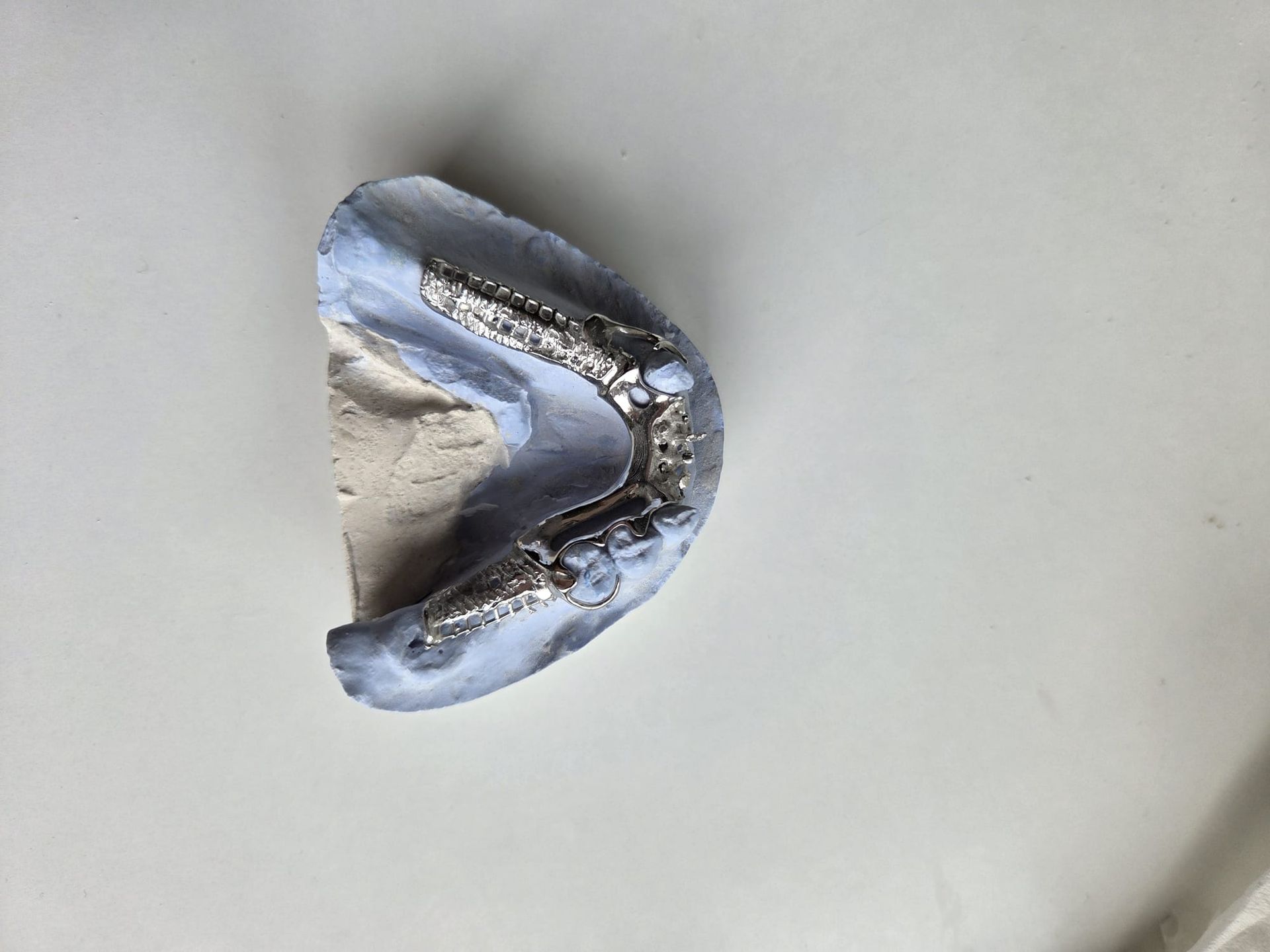 Primer plano de un objeto metálico plateado y curvo sobre una superficie gris claro