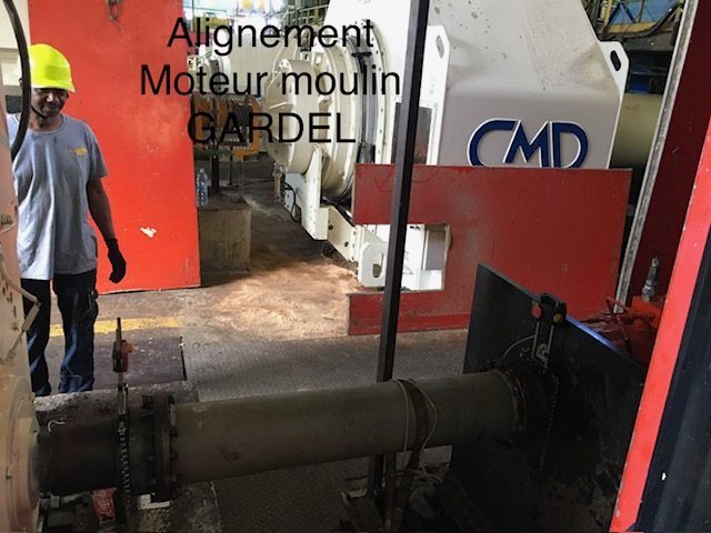 Machines d'atelier avec un ouvrier à côté d'un grand système de poulies de moteur d'alignement et d'un panneau d'équipement rouge.