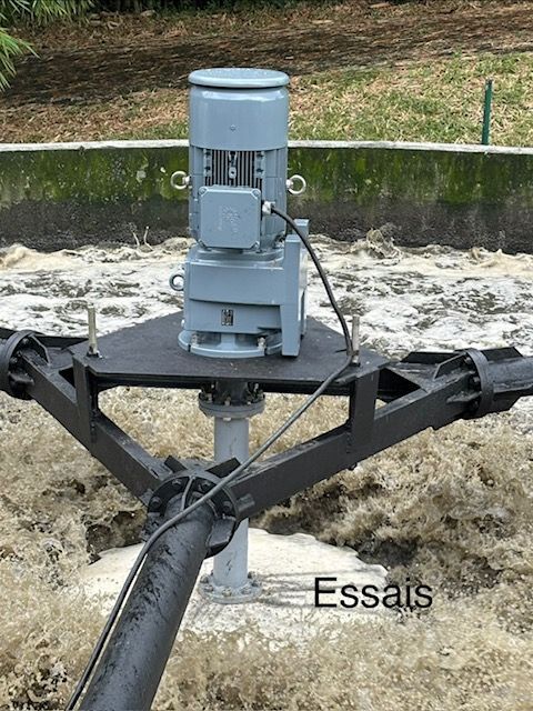 Machines motorisées grises avec bras noirs montées au-dessus d'une surface sablonneuse dans un bassin extérieur.