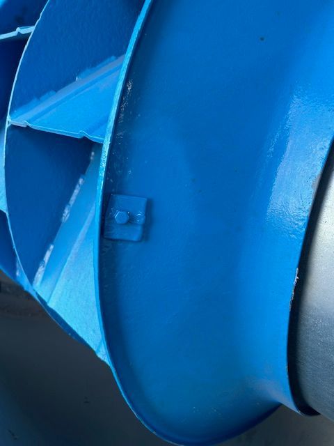 Gros plan sur une pièce de machine en métal bleu avec des ailettes inclinées et un bord cylindrique incurvé.