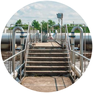 Vers assainissement Vue circulaire d'un escalier métallique menant à des réservoirs et des canalisations industrielles à l'extérieur.