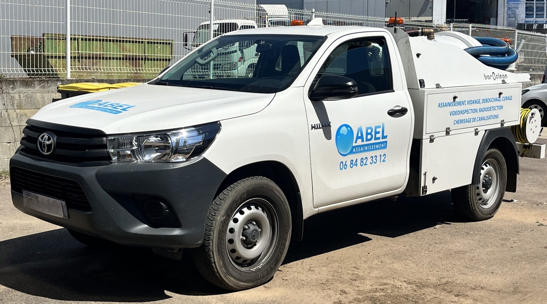 Camionnette utilitaire blanche avec logo bleu de l'entreprise garée à l'extérieur sur un terrain