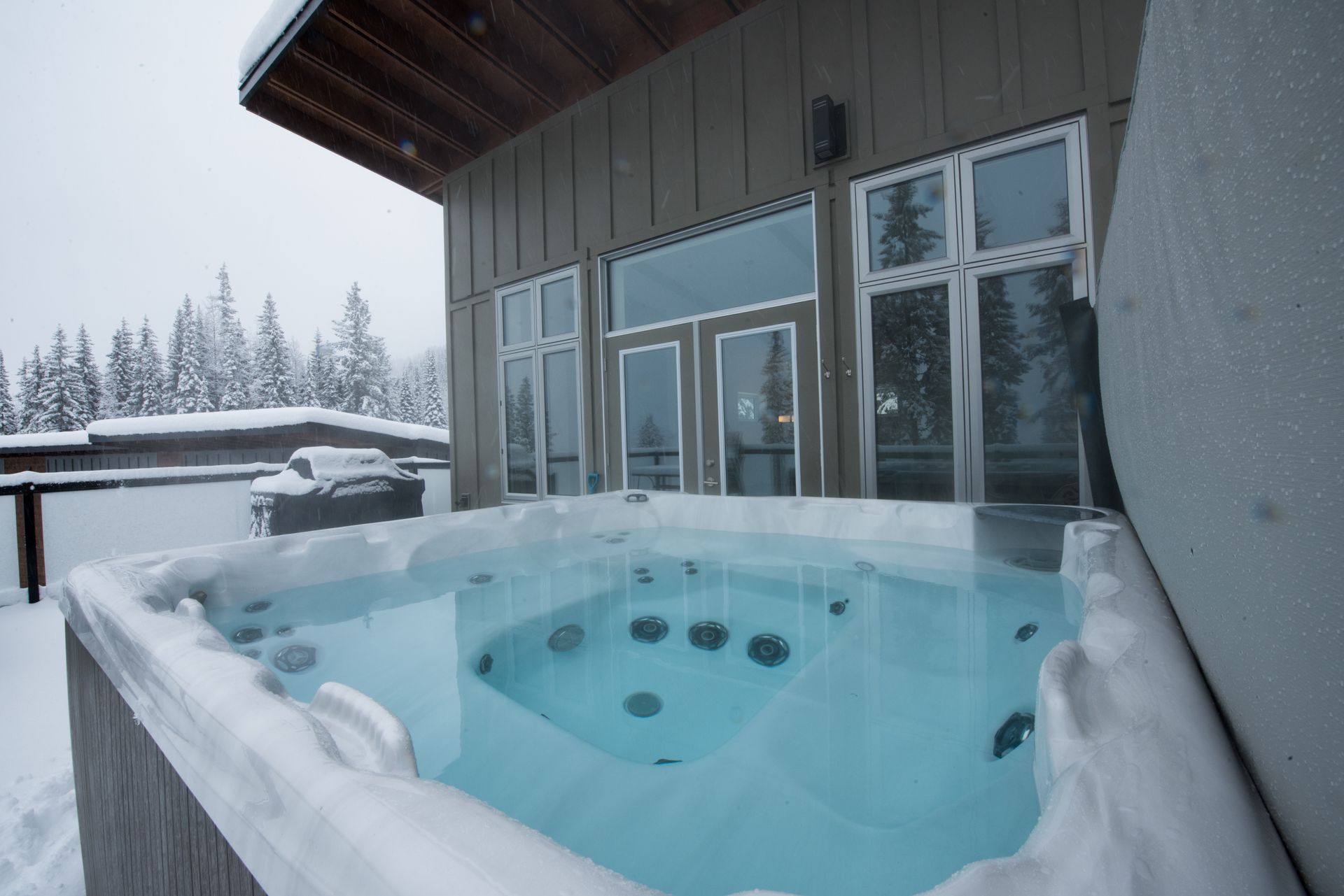 Snow-covered outdoor hot tub beside a modern building in winter