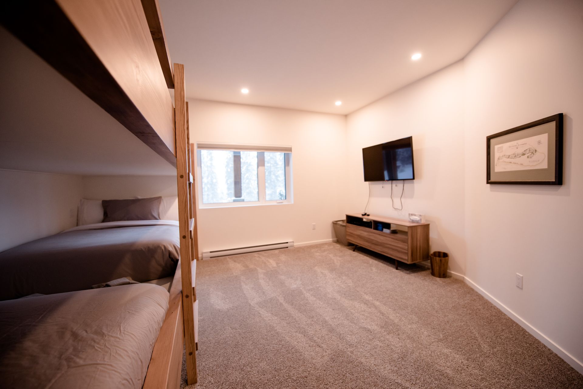 Spacious carpeted bedroom with bunk bed, window, wall-mounted TV, and dresser.