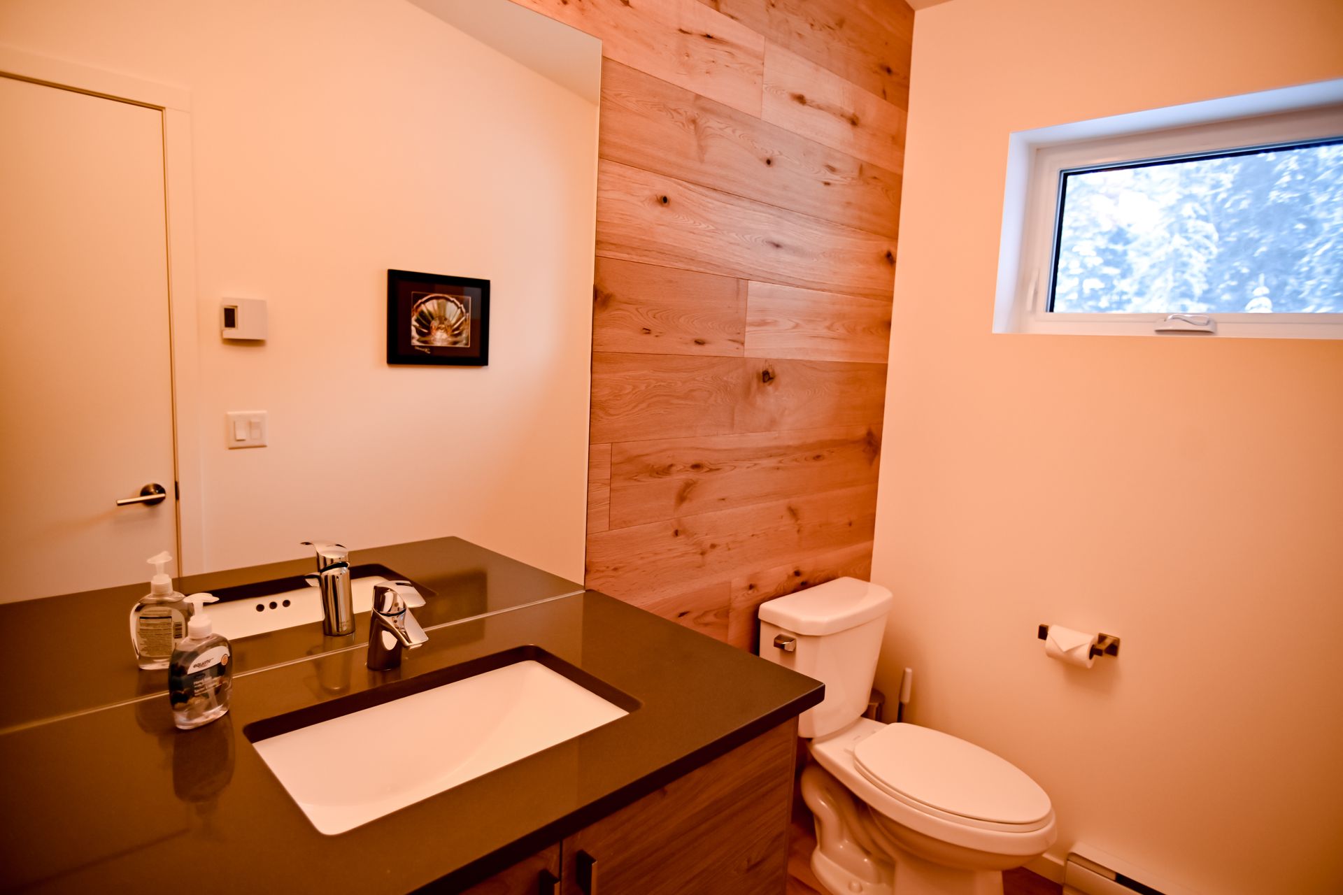 Modern bathroom with wood accent wall, sink vanity, toilet, and small window