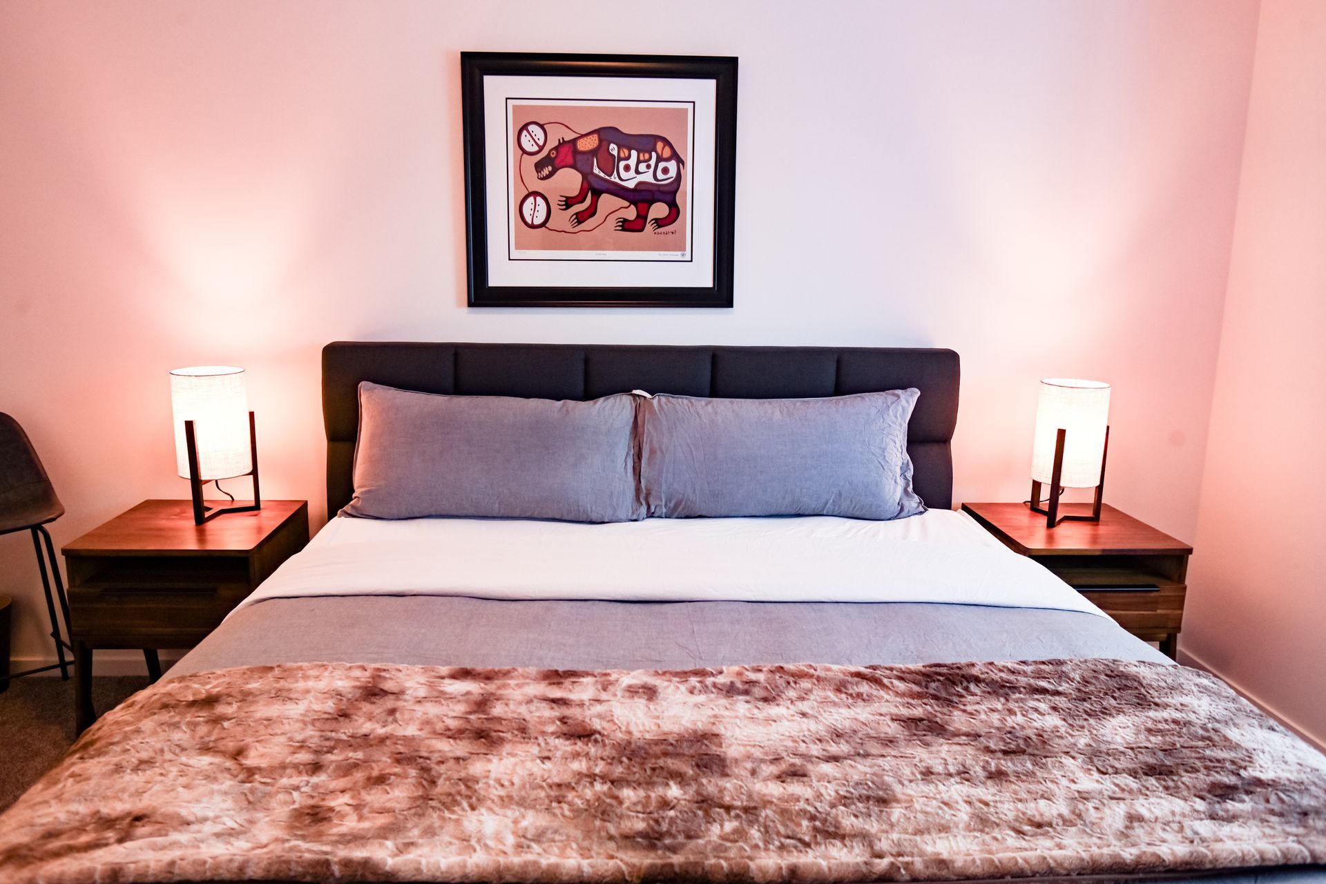 Neatly made bed in a softly lit bedroom with bedside lamps and framed wall art.