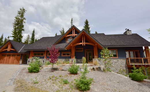 Rustic log cabin with wood beams, stone roof, and landscaped gravel front yard under cloudy sky