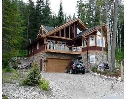 Rustic mountain cabin with garage and car, surrounded by tall pine trees