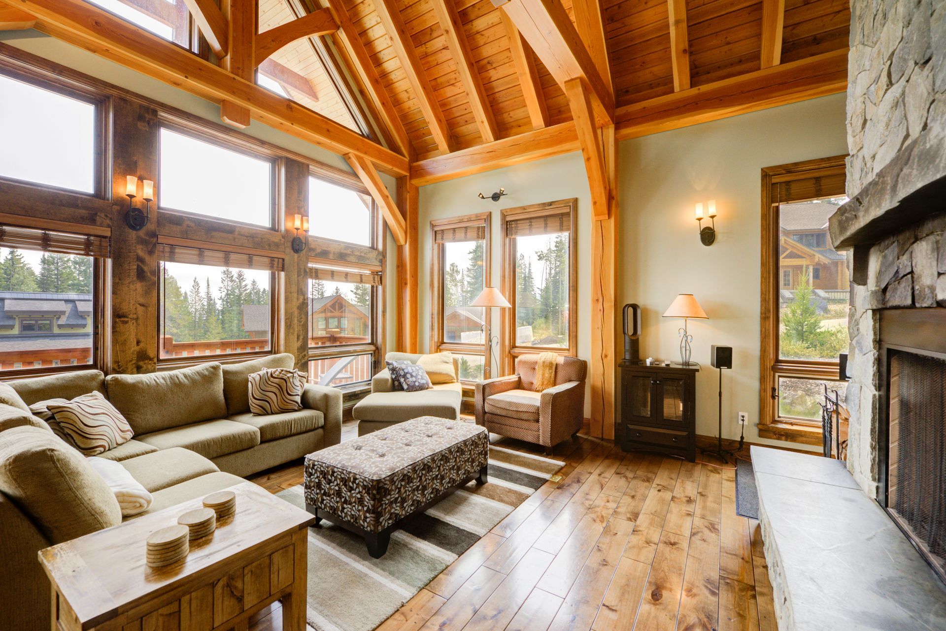 Cozy rustic living room with vaulted wood سقiling, large windows, sectional sofa, and stone fireplace