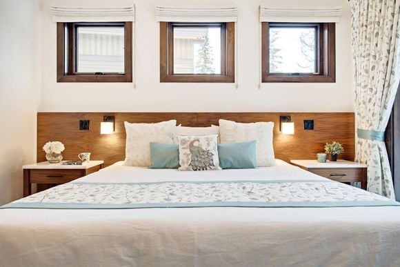 Bright bedroom with a neatly made bed, wooden headboard, and three windows above it