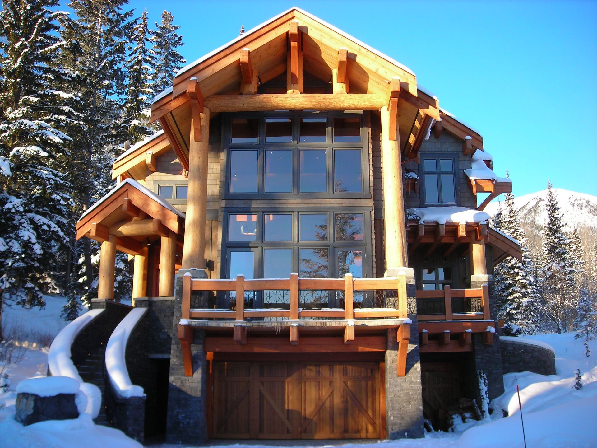 Snow-covered modern wooden chalet with large windows and a garage in a mountain setting