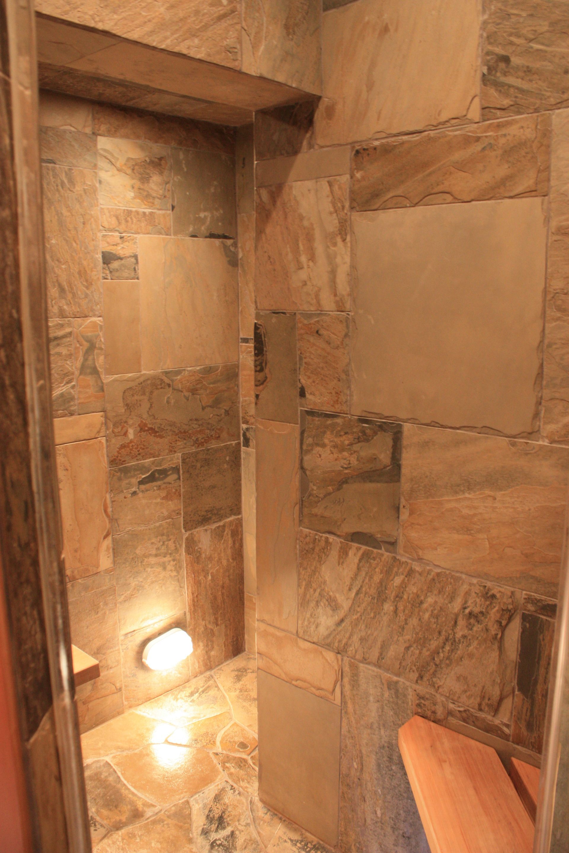 Stone shower with warm recessed lights and a wooden bench on the right