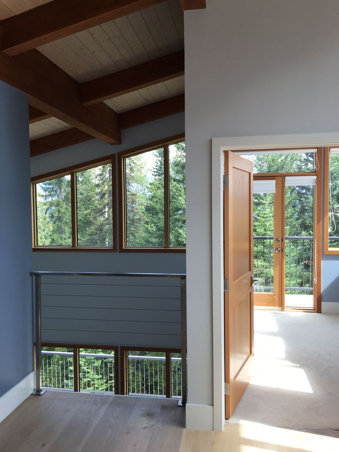Modern home interior with skylights, large windows, and an open doorway to a sunlit balcony.