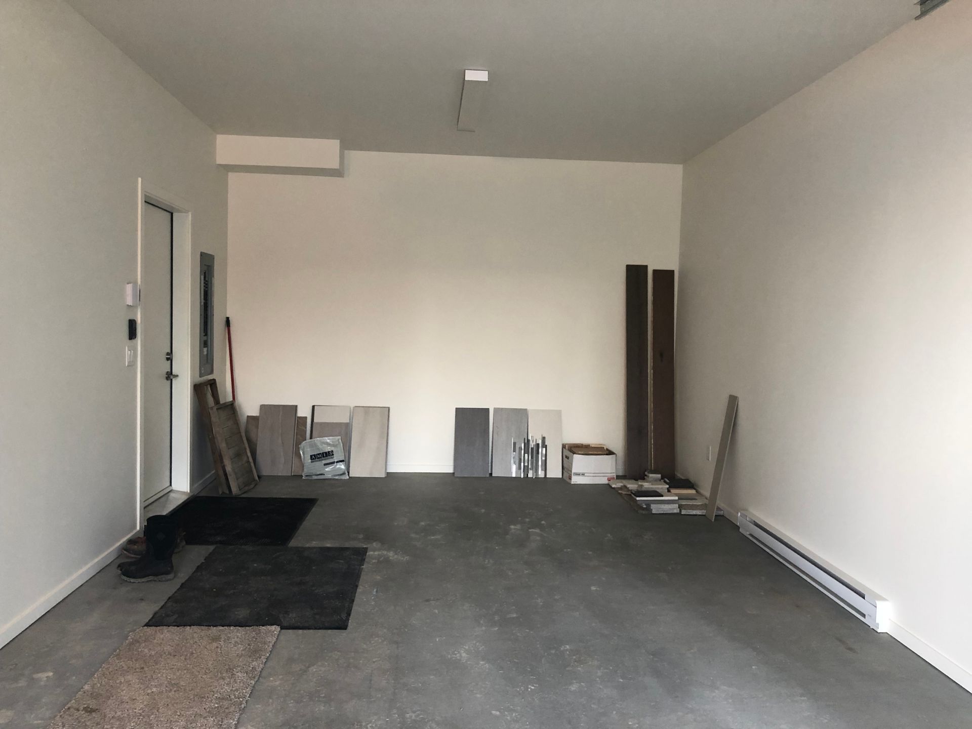 Empty garage with white walls, gray floor, and a few leaning boards and materials along the back wall