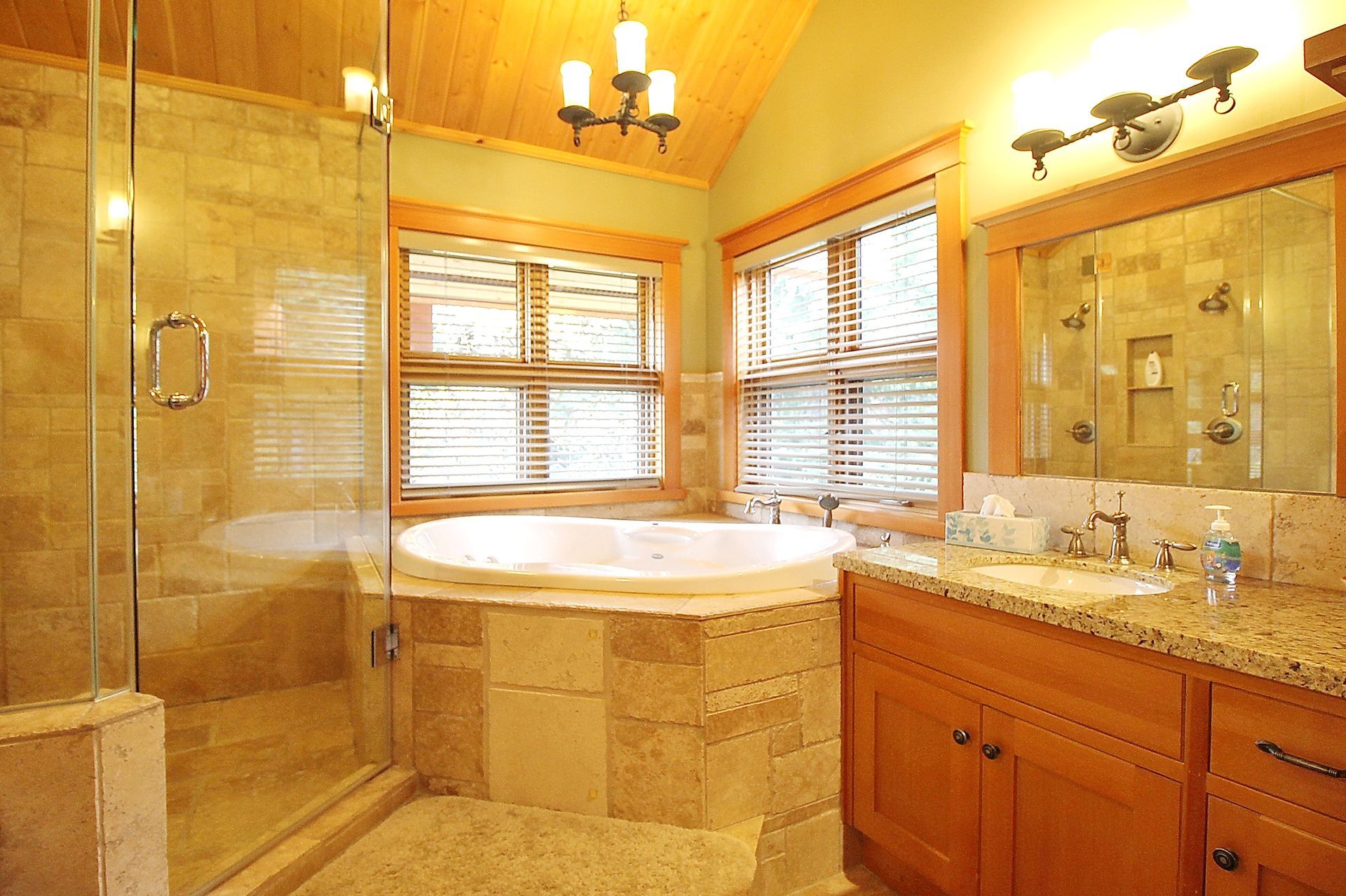 Luxury bathroom with a large soaking tub, glass shower, granite vanity, and warm beige tile.