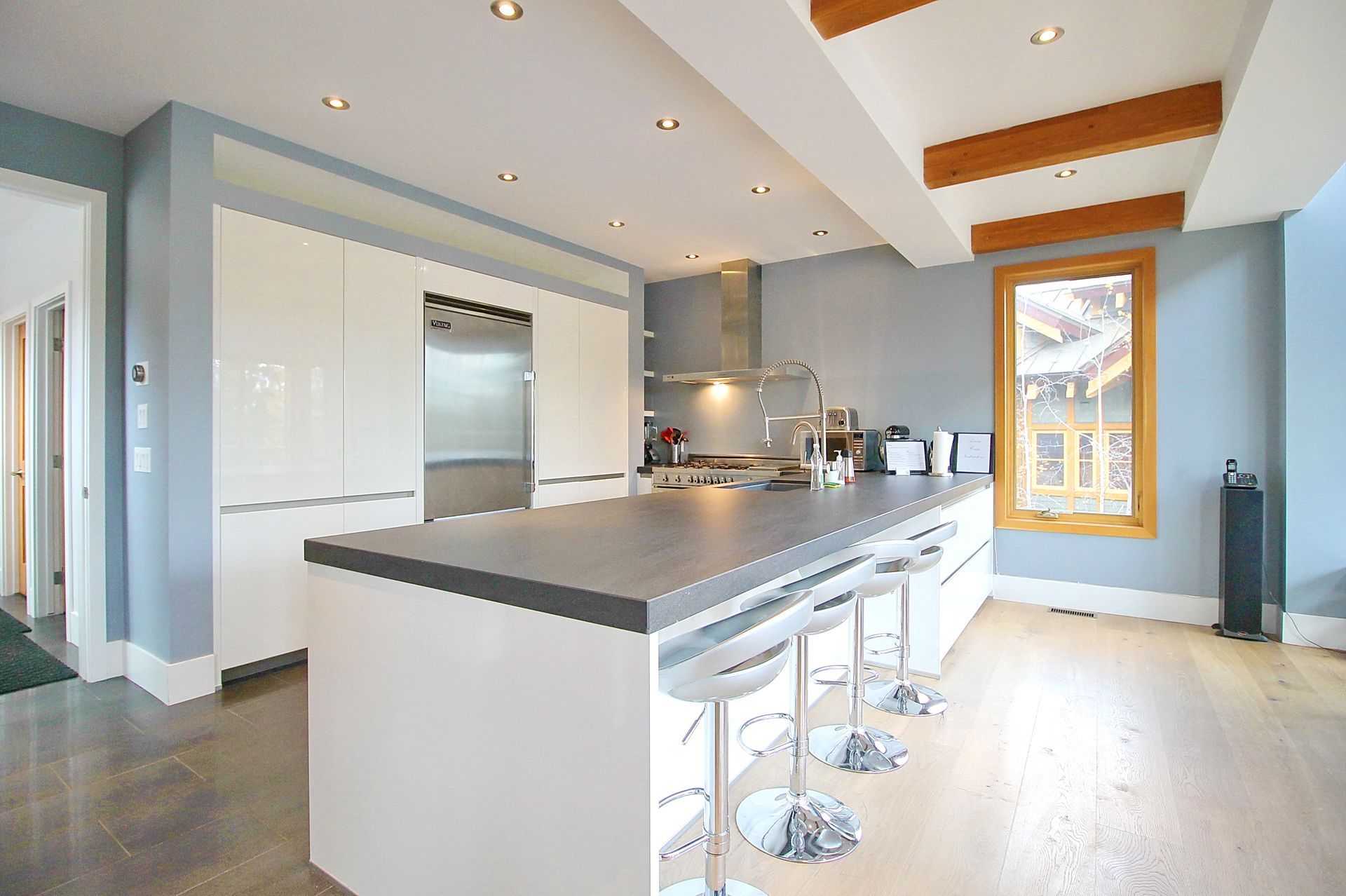 Bright modern kitchen with white cabinets, gray island, bar stools, and skylights.