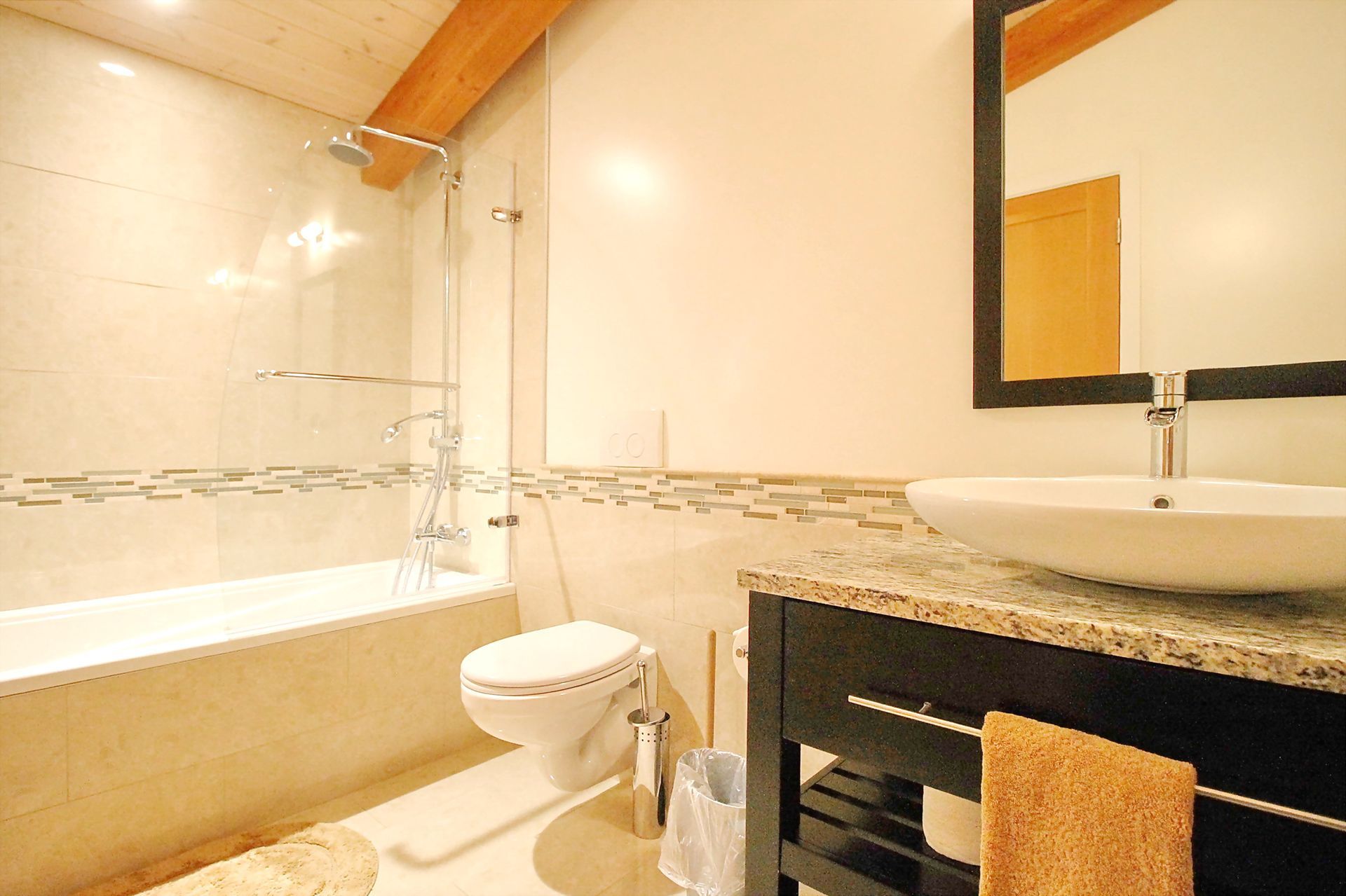 Bright bathroom with a bathtub, toilet, sink, and large mirror in beige tones.