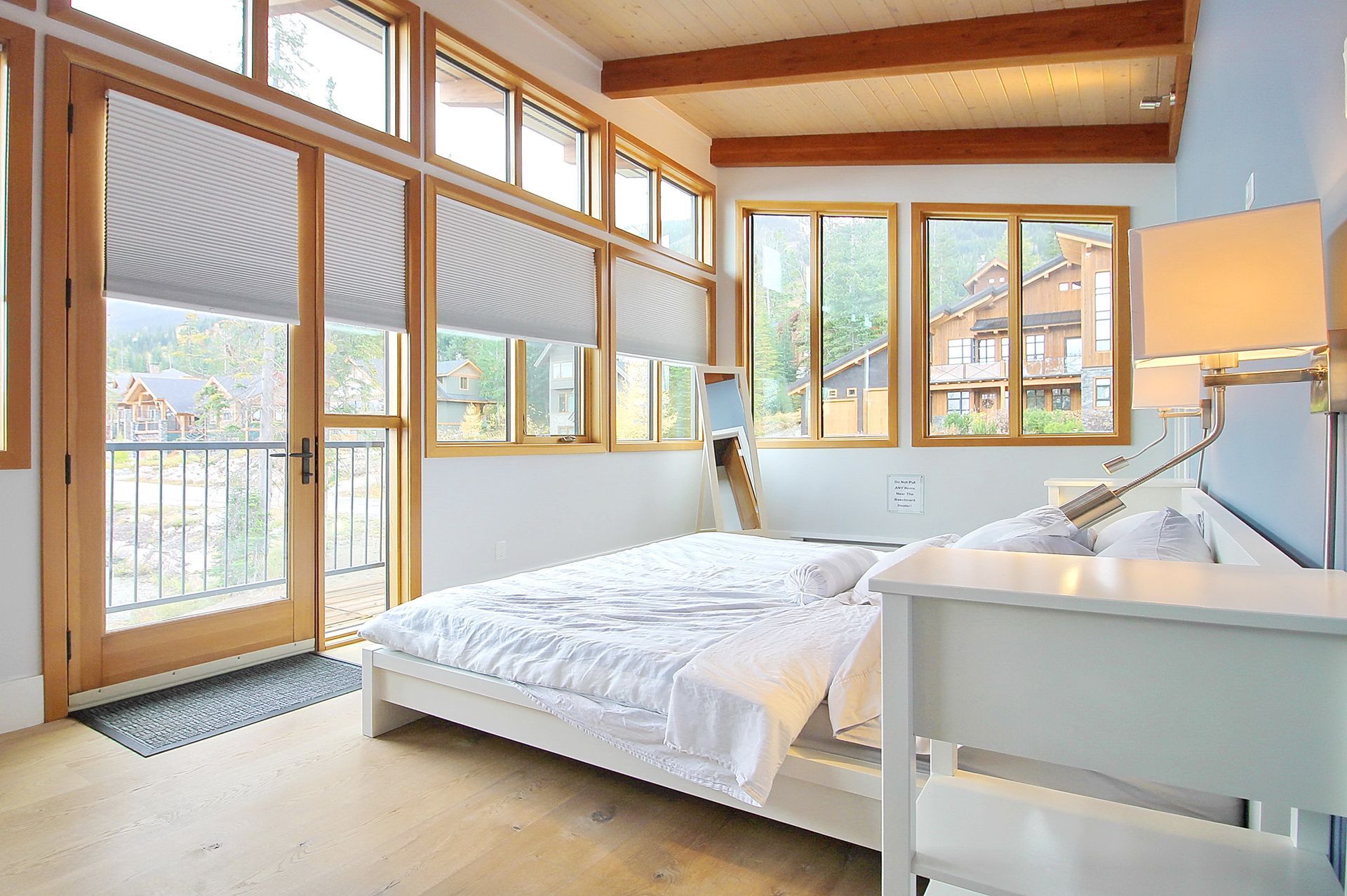 Bright bedroom with white bed, large windows, wood beams, and soft natural light